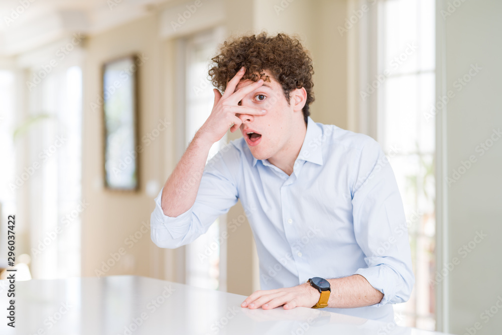 Young business man with curly read head peeking in shock covering face and eyes with hand, looking through fingers with embarrassed expression. Young business man with curly read head peeking in shock covering face and eyes with hand, looking through fingers with embarrassed expression.