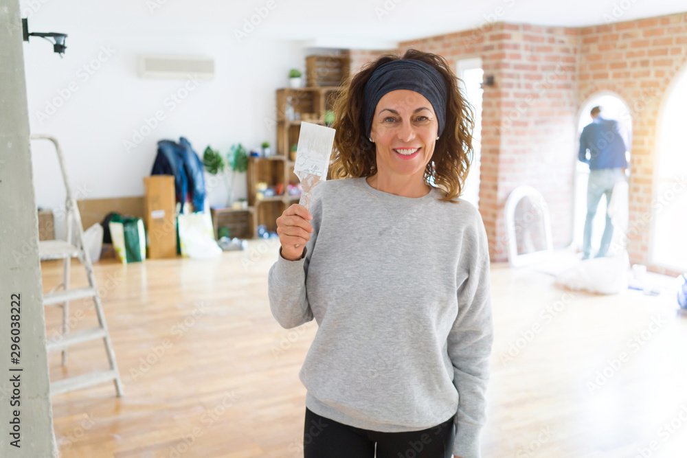 Middle age woman with curly hair smiling cheerful painting new house using paint brush, renovating and decorating the wall Middle age woman with curly hair smiling cheerful painting new house using paint brush, renovating and decorating the wall