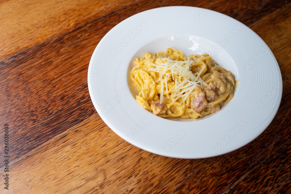 Delicious spaghetti, bacon topped with cheese, served on a white plate on brown wooden table top Delicious spaghetti, bacon topped with cheese, served on a white plate on brown wooden table top