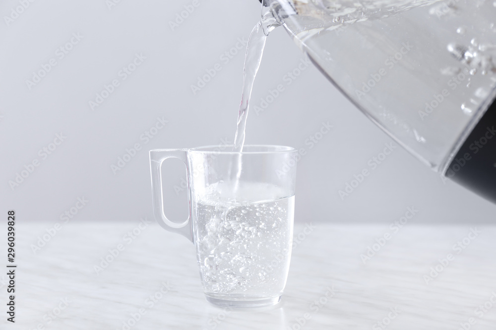 Pouring of boiled water from electric kettle into cup on table Pouring of boiled water from electric kettle into cup on table