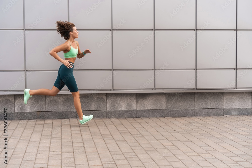 Fototapeta premium Sporty young woman athlete running on urban street in morning.