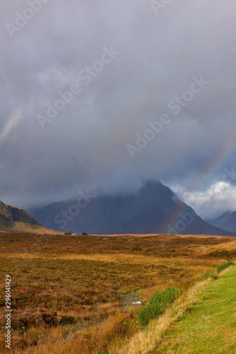 A rainbow between the sunlit moorland of Rannoch Moor and the dark cloud covered mountains of the Three Sisters, or Bidean nam Bian in Glencoe.