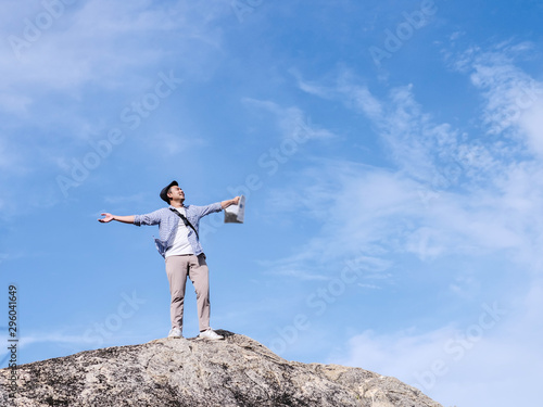 Asian tourist standing on the rock and raising hands with blue sky background,