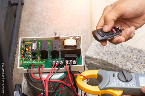 Technician man hand pressing remote control while repair and using digital clamp meter to test the function and  electrical current of motor bridge gear of auto garage.Maintenance and service concept