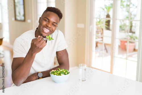 Photography Handsome african young man eating a healthy vegetable salad using a fork to eat