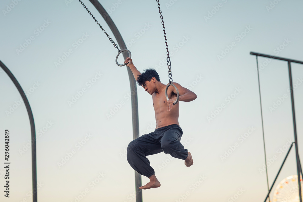 A young man athlete working out on traveling rings on muscle beach, Santa Monica, California