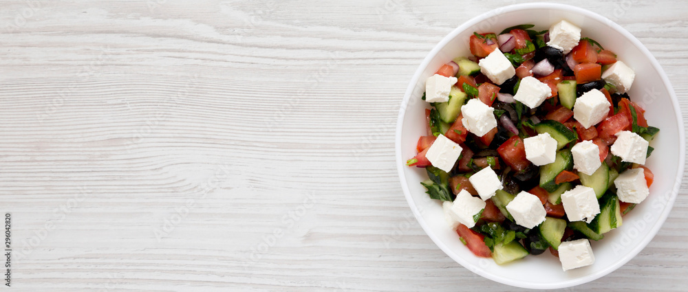 Homemade Shepards salad with cucumbers, feta and parsley in a white bowl on a white wooden background, overhead view. From above, overhead. Copy space. Homemade Shepards salad with cucumbers, feta and parsley in a white bowl on a white wooden background, overhead view. From above, overhead. Copy space.