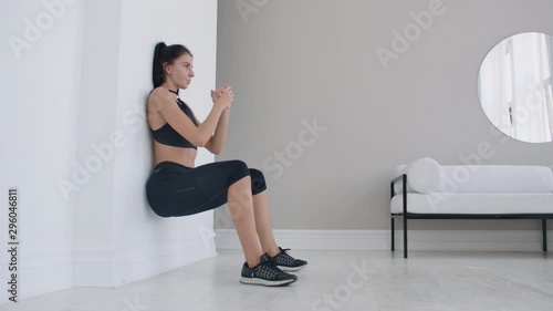 A woman in a static position carries out a grueling exercise leaning against a wall in a sitting position. Endurance training photo