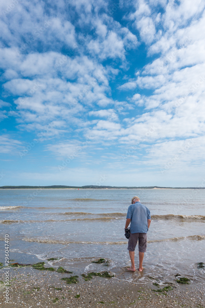 Un homme marchant dans la mer. Pêcher les coquillages. Ramasser les coquillages sur la plage. Touriste à la mer. Vacances à Oléron. Un touriste sur la plage, le ciel bleu, la mer, un nuage.
