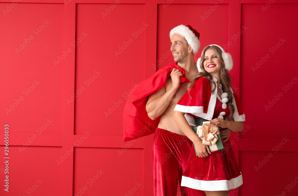 Fototapeta premium Young couple dressed as Santa Claus with Christmas gifts on color background