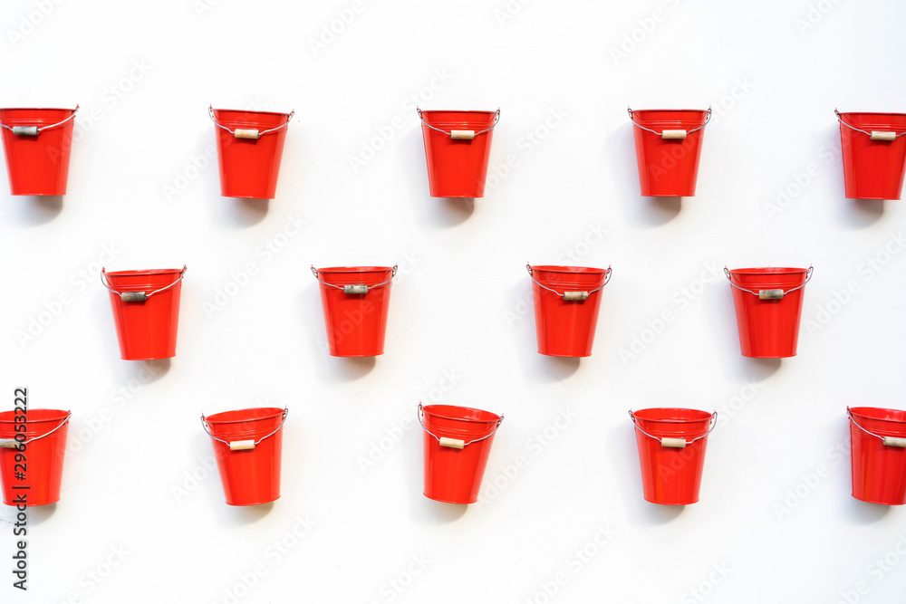 Several red color bucket with a wooden handle hang nailed on a white wall. Natural seamless pattern. Creative idea decorative concept Several red color bucket with a wooden handle hang nailed on a white wall. Natural seamless pattern. Creative idea decorative concept