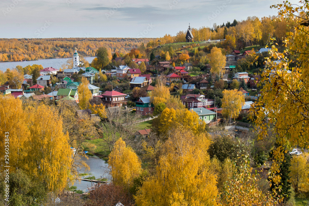 RUSSIA, Plyos - October 04, 2019: Ivanovo Region. Bright yellow autumn forest on background of Volga river. from height of Cathedral Mountain. Varvara church and colorful houses in autumn sunny day.