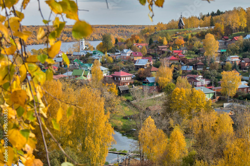 RUSSIA, Plyos - October 04, 2019: Ivanovo Region. Bright yellow autumn forest on background of Volga river. from height of Cathedral Mountain. Varvara church and colorful houses in autumn sunny day. photo