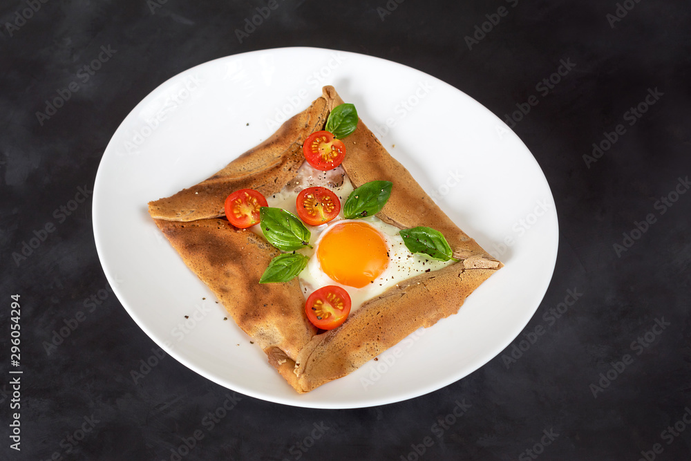 Galette bretonne with egg, tomatoes and basil on a black background. Galette bretonne with egg, tomatoes and basil on a black background.