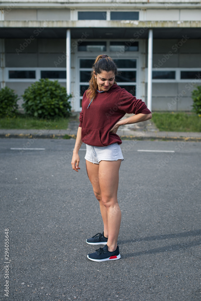 Young female athlete suffering from lower back pain while running on asphalt. Young female athlete suffering from lower back pain while running on asphalt.