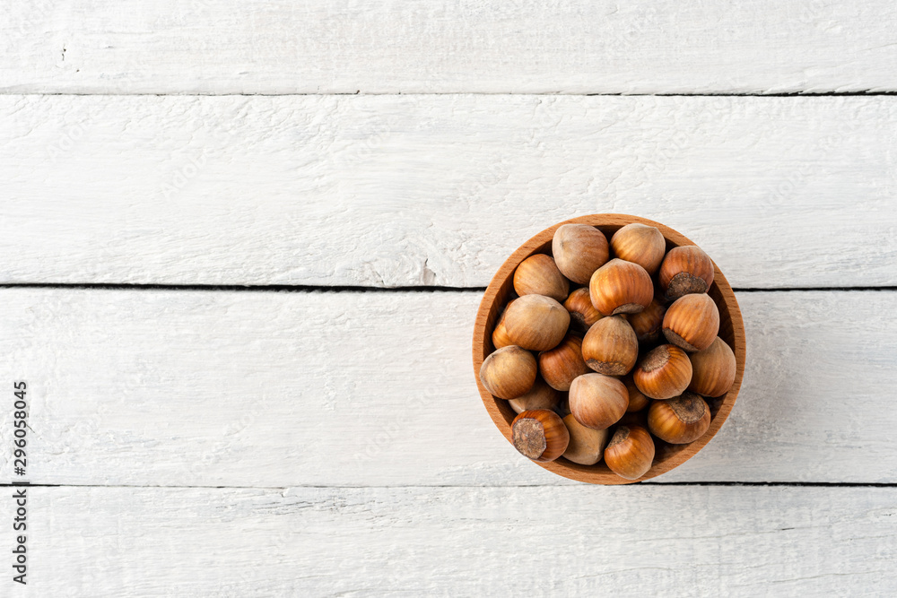 Overhead shot of hazelnuts in bowl on white wooden table. Healthy snacks - obrazy, fototapety, plakaty 