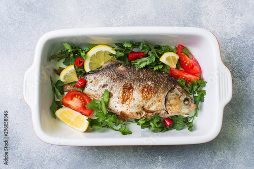 Baked carp fish with vegetables and spices in a baking tray.