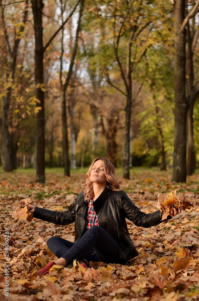 Beautiful woman sitting on the ground and throwing yellow leaves in park. Leisure time on warm autumn day. Autumn mood, enjoy the season Beautiful woman sitting on the ground and throwing yellow leaves in park. Leisure time on warm autumn day. Autumn mood, enjoy the season