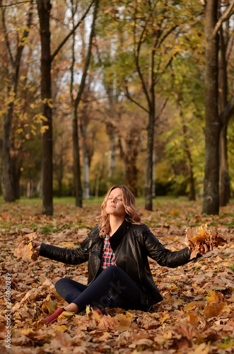Beautiful woman sitting on the ground and throwing yellow leaves in park. Leisure time on warm autumn day. Autumn mood, enjoy the season