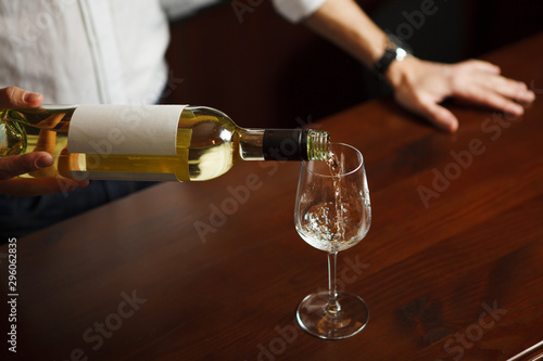 Fotografija Male sommelier pouring white wine into long-stemmed wineglasses.
