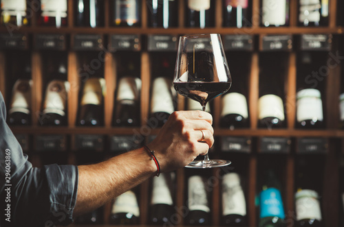 Close up shot of sommelier holding a glass of delicious red wine and excellent wine bottles collection on the background.