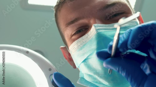 young handsome smiling doctor dentist in mask holds medical lamp and uses dental mirror during patient's examination