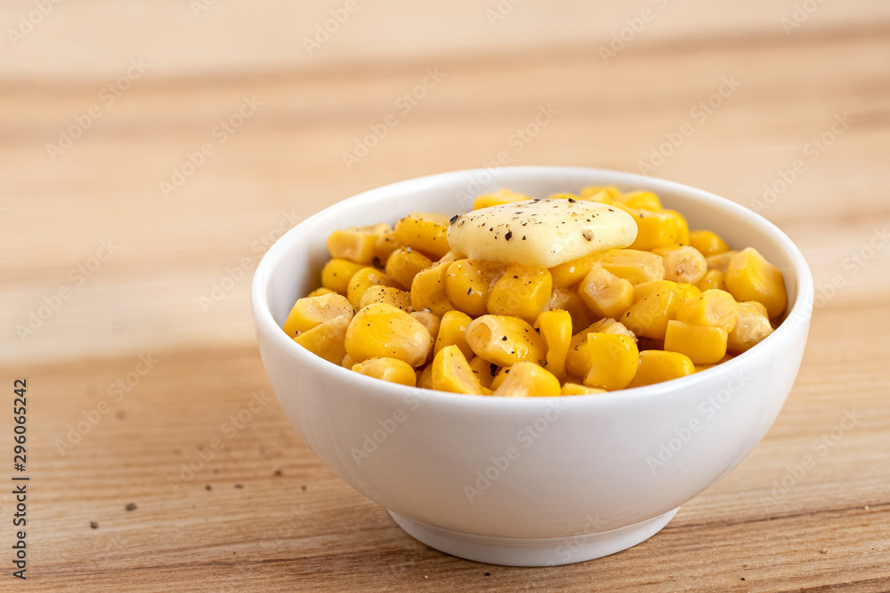 Canned sweet corn with a knob of butter and ground black pepper in a white ceramic bowl isolated on light wood. Space for text. Canned sweet corn with a knob of butter and ground black pepper in a white ceramic bowl isolated on light wood. Space for text.