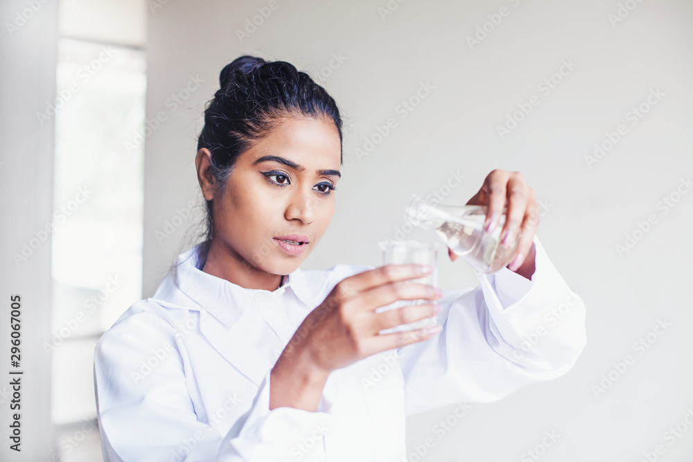 Young Indian biotechnology science student pouring water into a flask for a scientific experiment Young Indian biotechnology science student pouring water into a flask for a scientific experiment