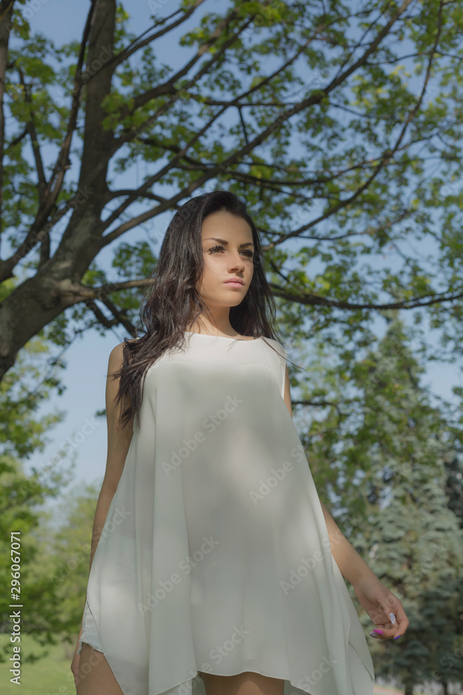 Attractive brunette woman in white dress posing in spring park Attractive brunette woman in white dress posing in spring park
