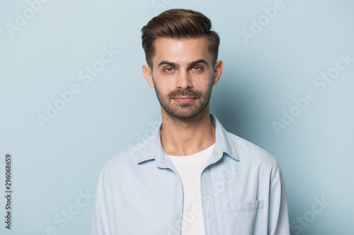 Headshot of serious caucasian young man posing on blue background © fizkes