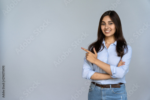 Confident smiling indian young woman professional student customer saleswoman looking at camera pointing at sales copy space isolated on grey studio background, happy lady showing aside portrait