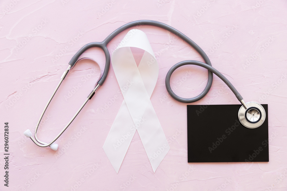 Fototapeta premium White awareness ribbons with stethoscope over slate on pink background