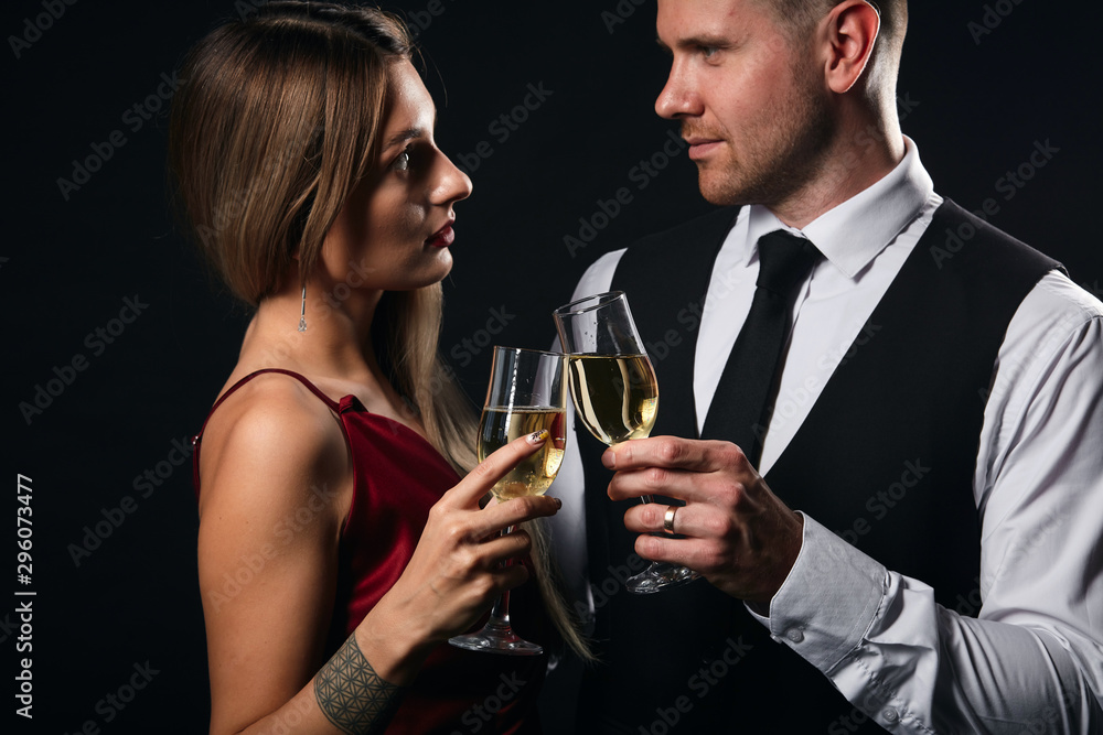 young elegant woman in red dress and handsome man in white shirt, tie enjoying spending time in the party, isolated black background, relationship. love young elegant woman in red dress and handsome man in white shirt, tie enjoying spending time in the party, isolated black background, relationship. love