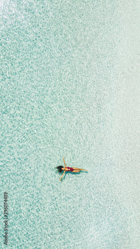 Slim tan young woman lying on turquoise clear water surface. Tropical island and luxury vacations concept. 16:9 for phone screen saver wallpaper.