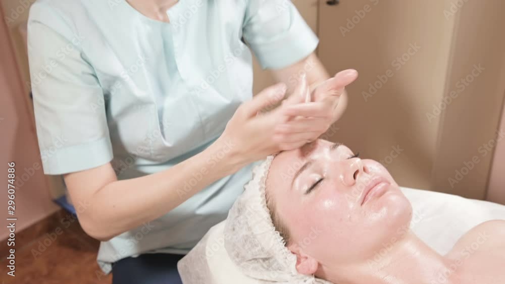 Girl beautician in a mask and gloves makes a salubrious facial massage to an attractive woman. New generation cosmetology massage Girl beautician in a mask and gloves makes a salubrious facial massage to an attractive woman. New generation cosmetology massage