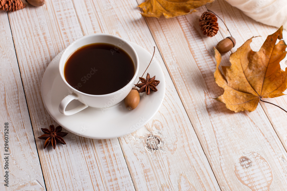 White scarf, cup of coffee and dry yellow leaves on a wooden table. Autumn mood, copy space.