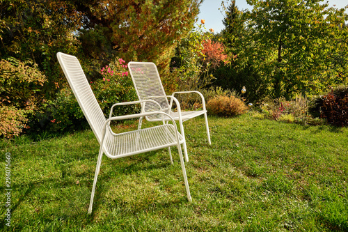 Two white garden chairs are standing in an idyllic green sunny October garden in Germany