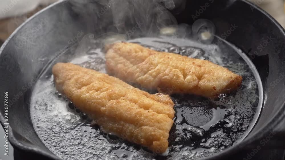 Slow motion of breaded fish fillets frying in butter in a cast iron