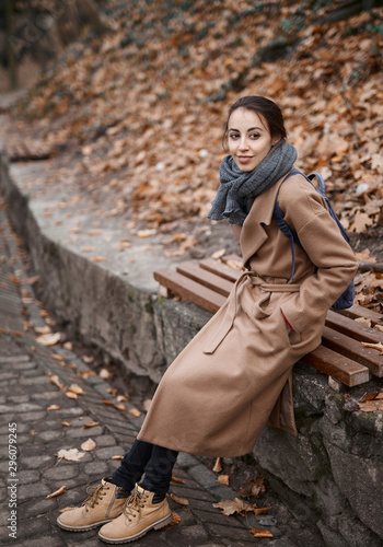 Autumn outdoor portrait of beautiful young woman in autumn park, sitting on a bench and enjoying the fall landscape. © vitaliymateha