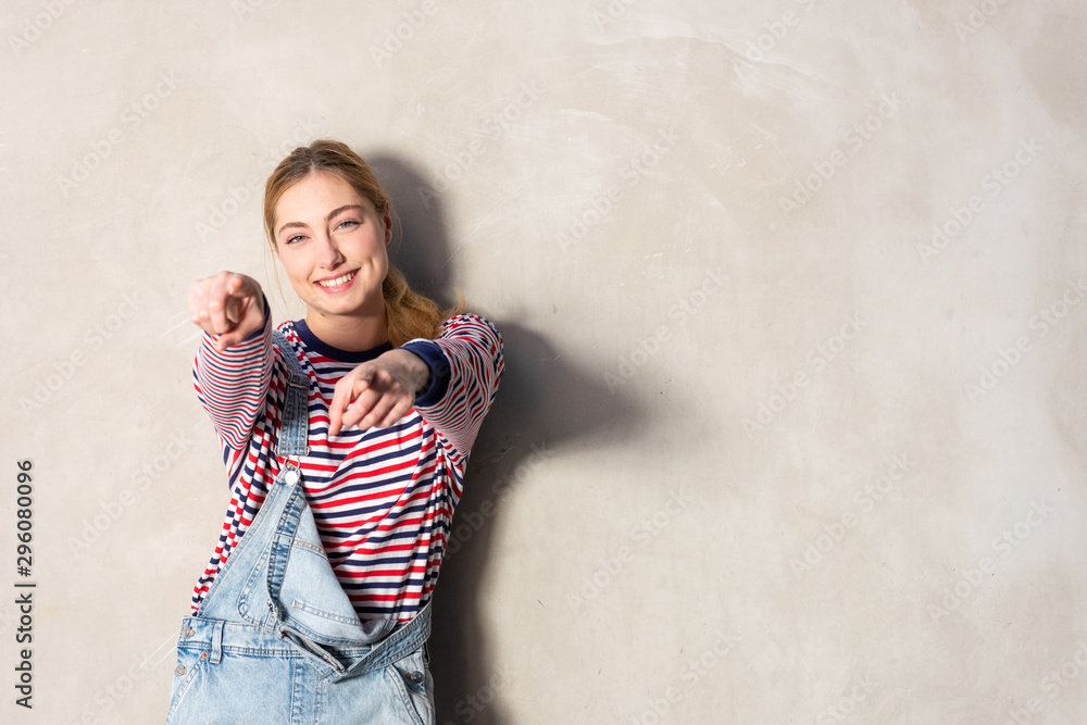 fun blond girl smiling and pointing fingers by gray background fun blond girl smiling and pointing fingers by gray background