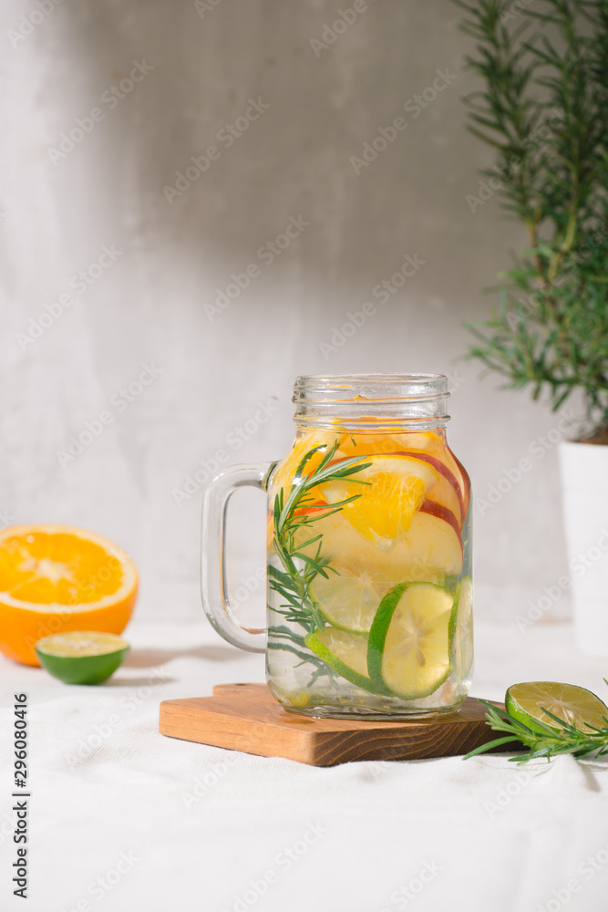 Detox water with lime, organe, apple and rosemary in a mason jar glass with a white wooden background Detox water with lime, organe, apple and rosemary in a mason jar glass with a white wooden background