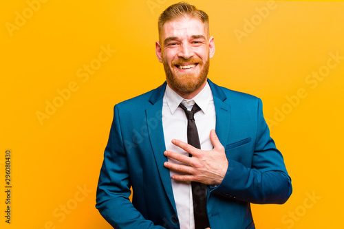 young red head businessman laughing out loud at some hilarious joke, feeling happy and cheerful, having fun against orange background