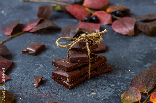 Pieces of dark chocolate and fall leaves on a dark background. Candy sweet dessert and snack. Dark chocolate is an antioxidant and boosts energy and serotonin. Close up, copy space