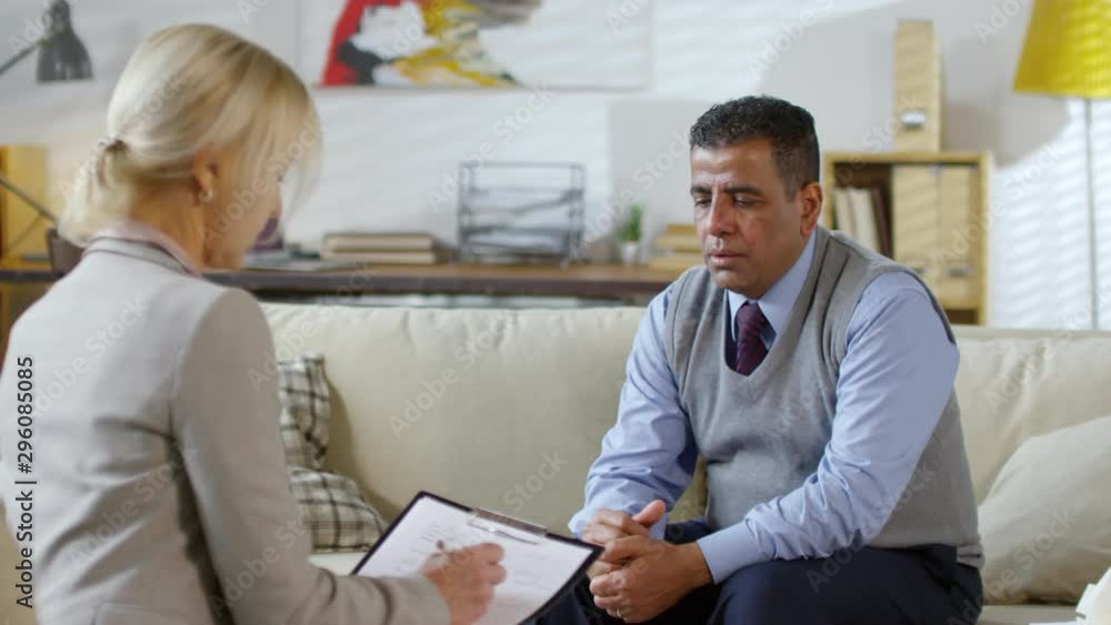 Upset middle-aged man of middle eastern ethnicity sitting on sofa and speaking with professional female psychologist during therapy session Upset middle-aged man of middle eastern ethnicity sitting on sofa and speaking with professional female psychologist during therapy session
