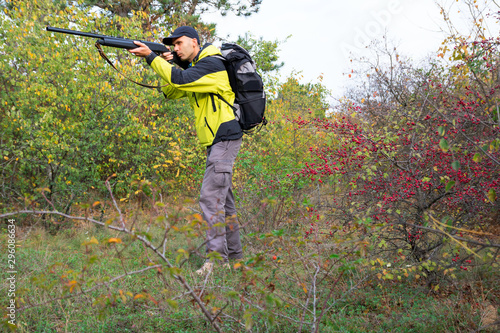 man with semi-automatic shotgun and backpack is hunting in the autumn forest