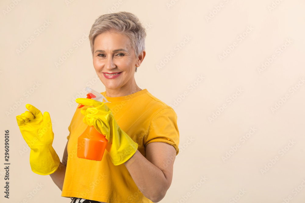 beautiful stylish woman aged, in a yellow T-shirt and rubber gloves on a beige background with detergent beautiful stylish woman aged, in a yellow T-shirt and rubber gloves on a beige background with detergent