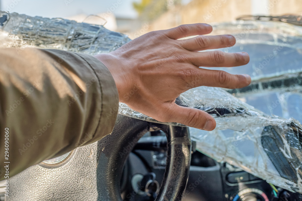 A man's fist against the broken windshield. Cracks on the windshield of the car from the impact