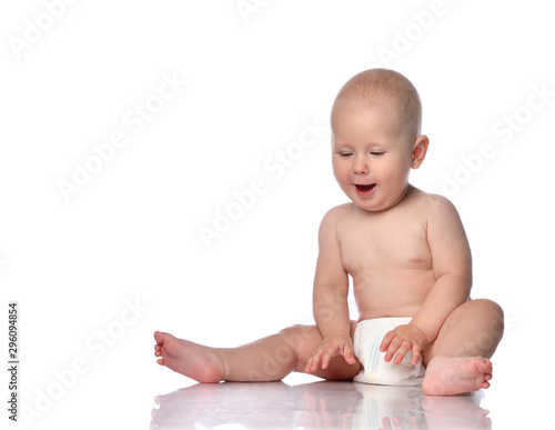 Happy infant child baby boy toddler in diaper is sitting  looking at something on the floor in front of him on white 