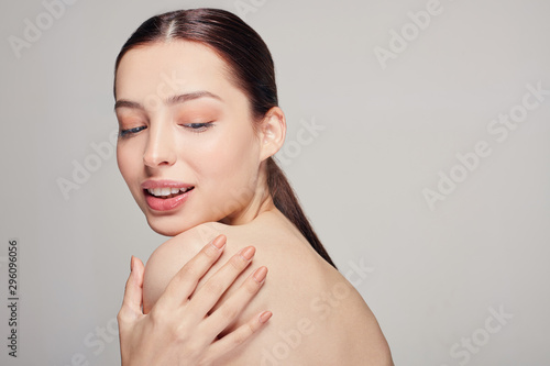 Young beautiful girl with blue eyes and full lips holds a hand on his shoulder. Looking down and smiling. Natural beauty.