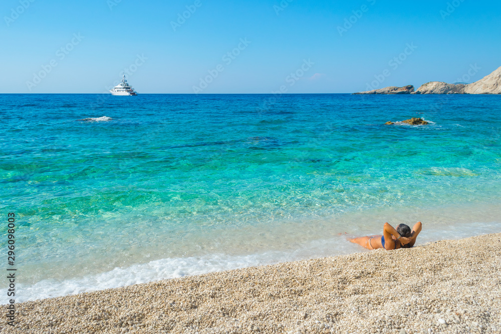 A girl is lying on the beach enloying the view of turquoise waters of the ocean at Petani beach in Kefalonia, Greece
